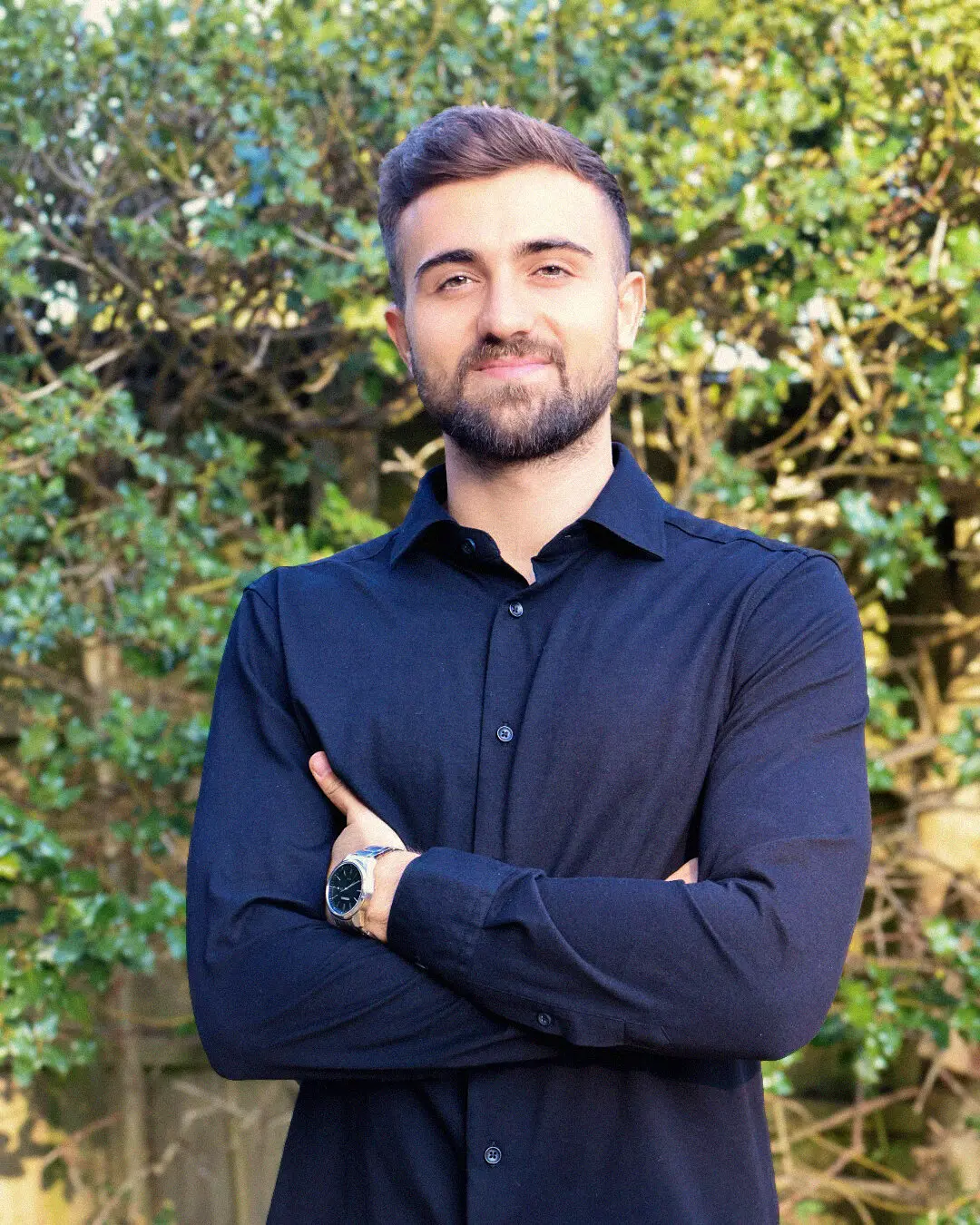 Alessandro Romanelli, founder of Slice 'N Vibe, arms crossed in a navy shirt in front of a garden hedge