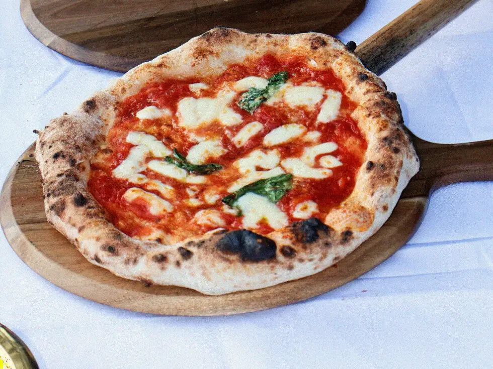 A freshly fired Neapolitan margherita on a board with the peel alongside
